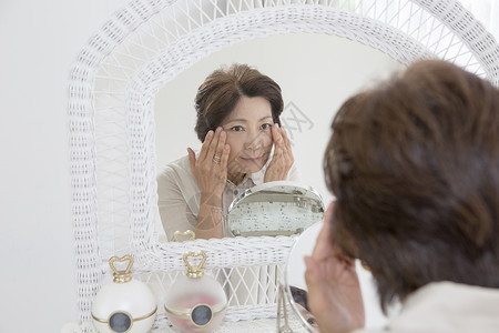 老年女性镜子前查看脸上的皱纹担心高清图片素材