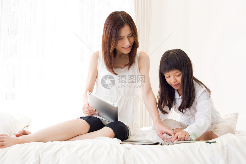 母亲和小孩在床上看画册图片