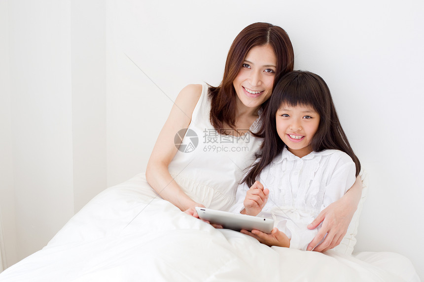 母亲搂着女儿躺在床上看平板电脑图片
