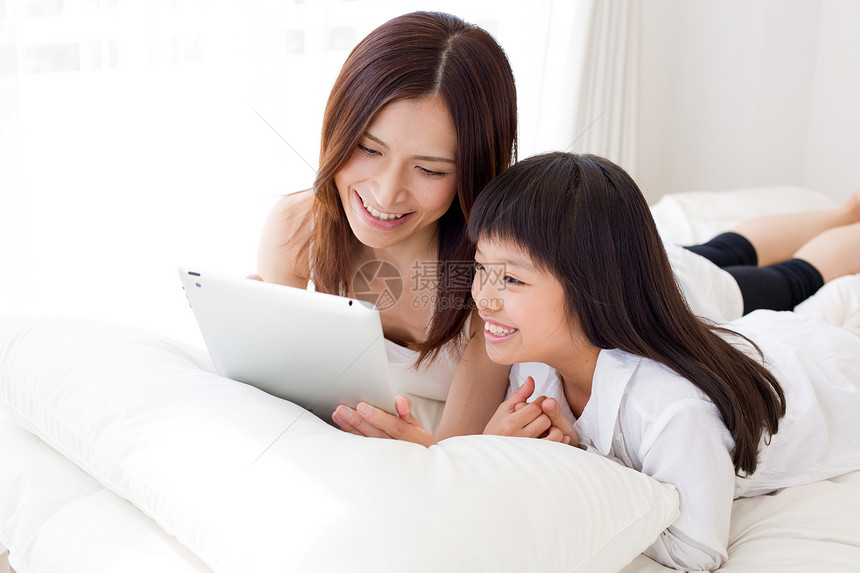 小女孩和母亲趴在床上使用平板电脑图片