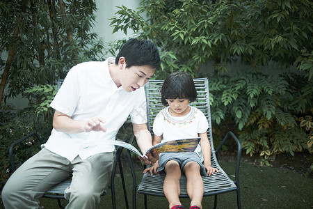爸爸陪伴女孩在花园里看书图片