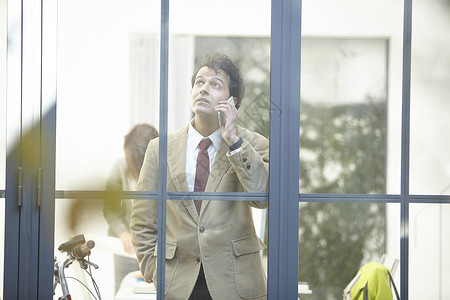 商业男士站在办公室窗边打电话图片