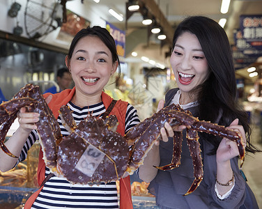 在市场上拿着螃蟹拍照的2个人图片