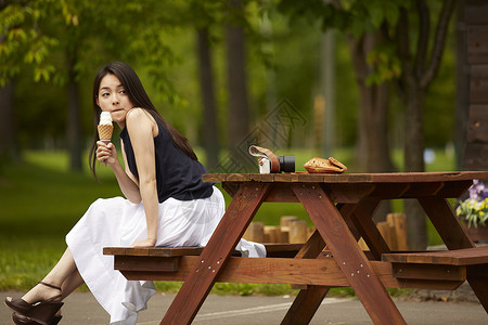 坐在公园木凳上吃冰激凌的长发美女图片