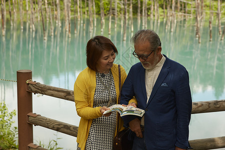 靠在湖边木围栏上看书的夫妇双人高清图片素材