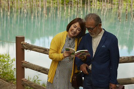 中年夫妇在湖边互相依偎着看一本书度假高清图片素材