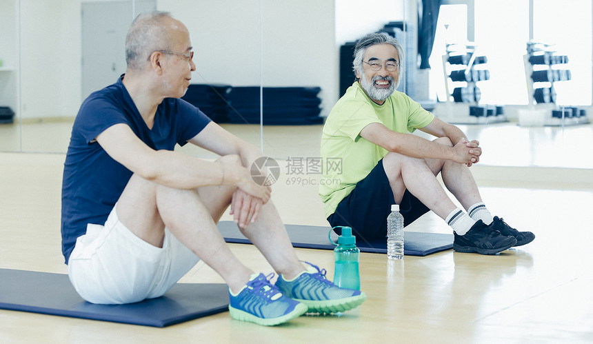 在健身房瑜伽垫上相视一笑的中年男人图片