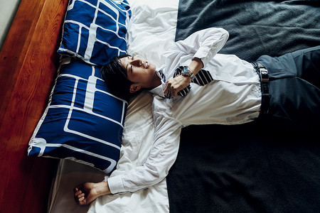 穿着衬衫领带躺在床上的年轻男性疲劳高清图片素材