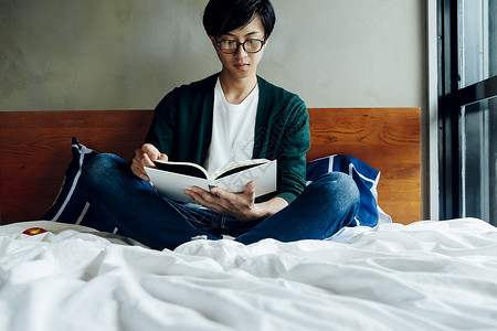 坐在床上看书的男子图片
