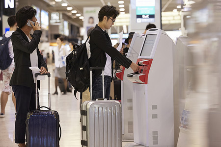 两个男人在机场拖着行李箱在自助机器取票背景图片