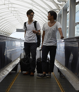 两个男人拖着行李箱走在机场电梯上图片
