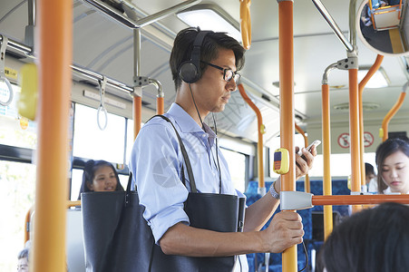 戴耳机坐公交车的男性职员高清图片素材