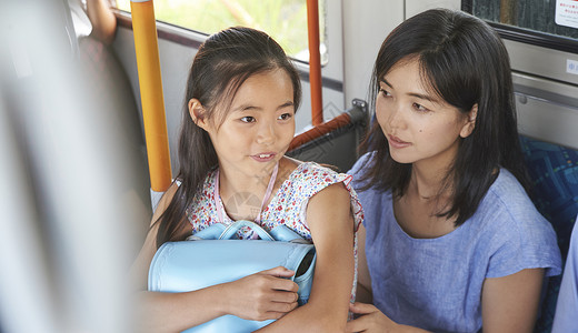 公交车上坐在母亲腿上的小学生女孩高清图片素材