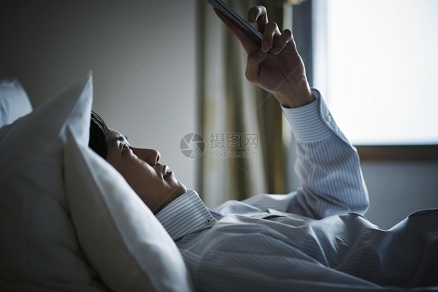躺在旅馆床上休息看手机的商务人士图片