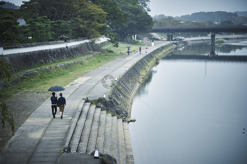 撑伞走在河堤边的年轻情侣的背影图片