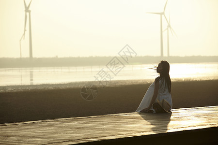 日落时女人坐在湿地栈道的剪影图片