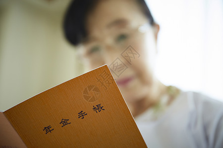 独居老妇人戴着眼镜看年金手账本背景图片