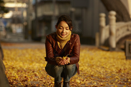 女人蹲在地上捧着银杏叶风景名胜高清图片素材