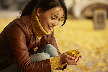 女人蹲在地上捧着银杏叶假日高清图片素材