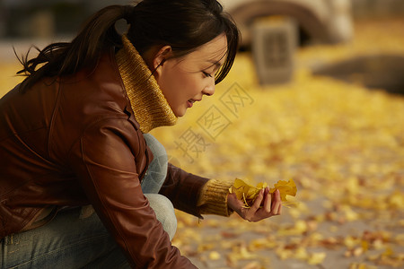 女人蹲在地上捧着银杏叶倾斜高清图片素材