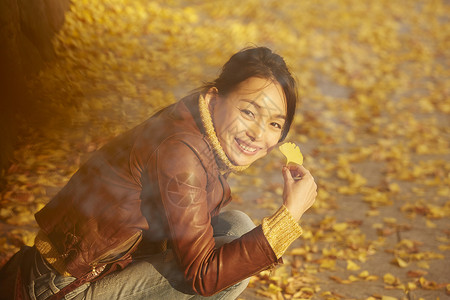 女人蹲在地上拿着银杏叶户外高清图片素材