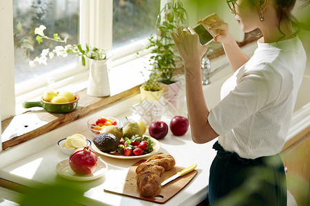 在窗边料理台制作午饭拍照的女人背景图片