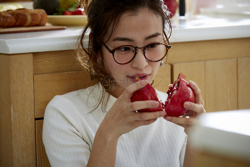 在窗边料理台蹲下看切开的石榴的女人图片