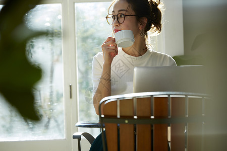 女人坐在窗边的桌上喝咖啡工作观叶植物高清图片素材