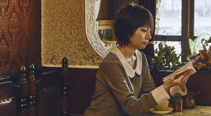 在咖啡馆里看书喝茶的年轻女性图片