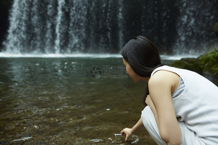 站在小溪边享受瀑布的女人在用杯子装溪水