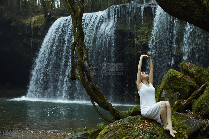年轻女性坐在小溪旁的岩石上伸展图片