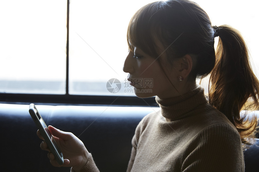 在窗边看手机思考的女性图片