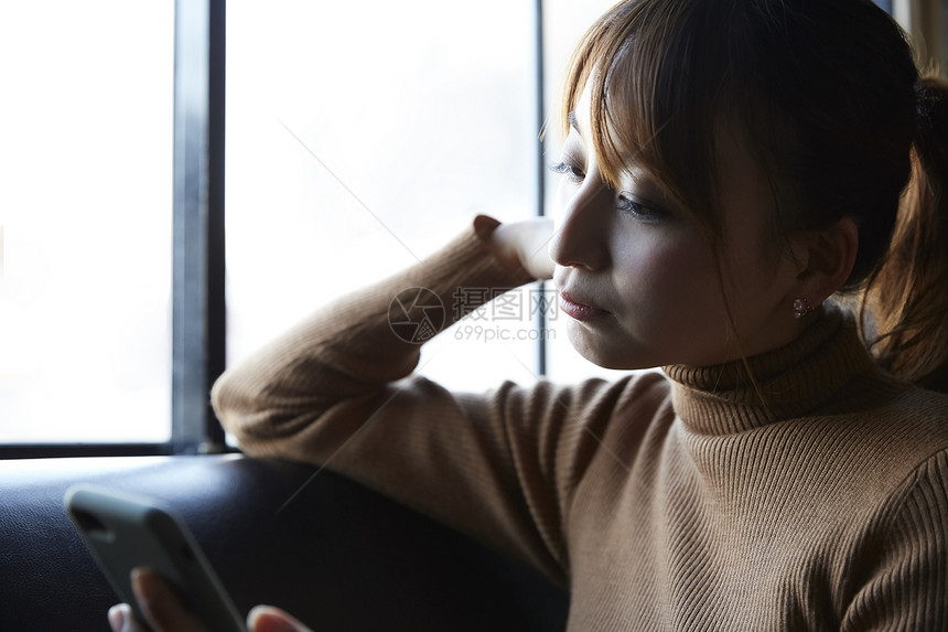 在窗边看手机思考的女性图片