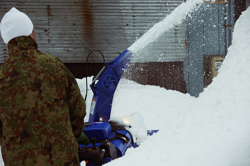 户外积雪使用除雪机的男性背影图片