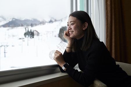 在窗边看雪景的女性图片