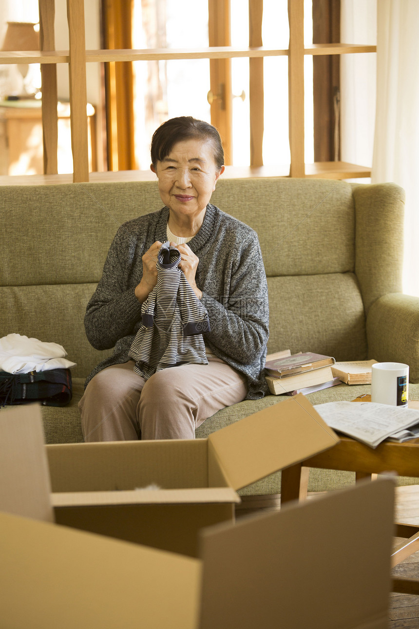 坐沙发上收纳整理衣服准备搬家的老年妇女图片