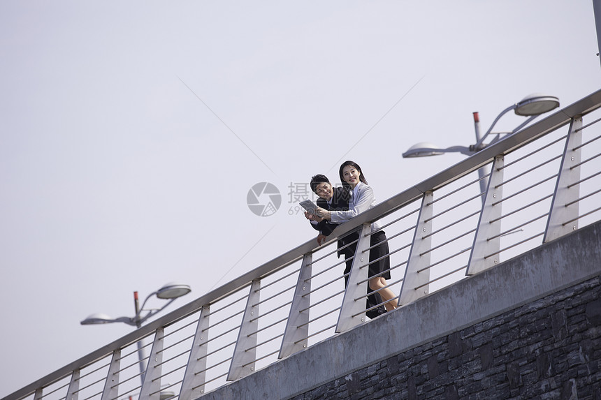 商务都市男女趴在机场天桥栏杆上讨论工作图片