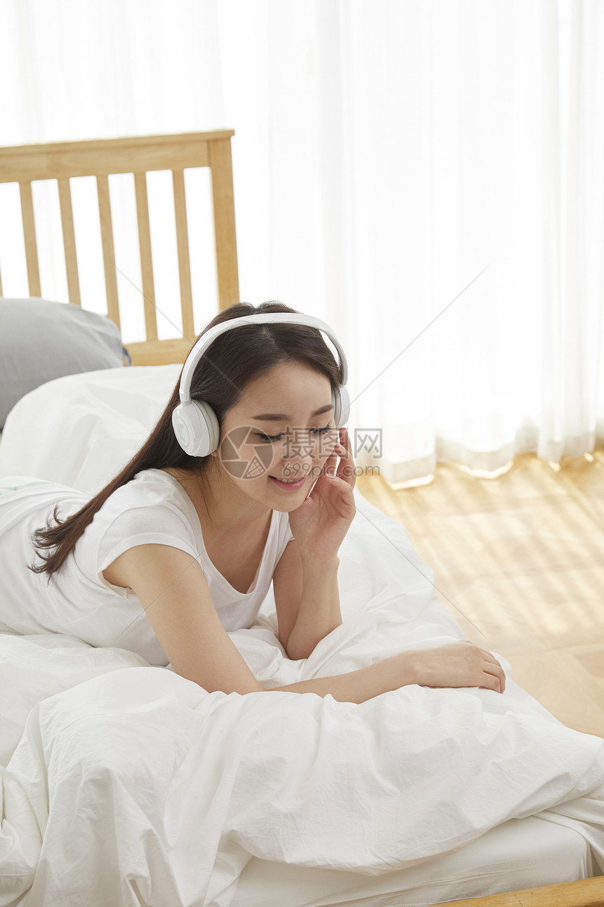 坐在床上带着耳机听音乐放松的女性图片