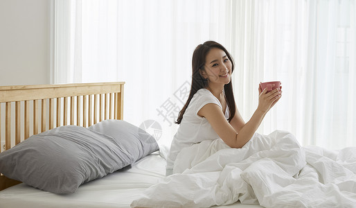 床上捧着咖啡微笑的居家女性卧室高清图片素材