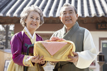 民俗村穿着传统服装拿着礼物盒微笑的夫妇图片