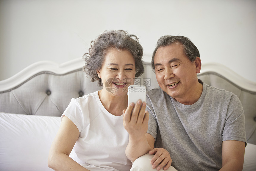 卧室里看着手机微笑的老夫妇图片