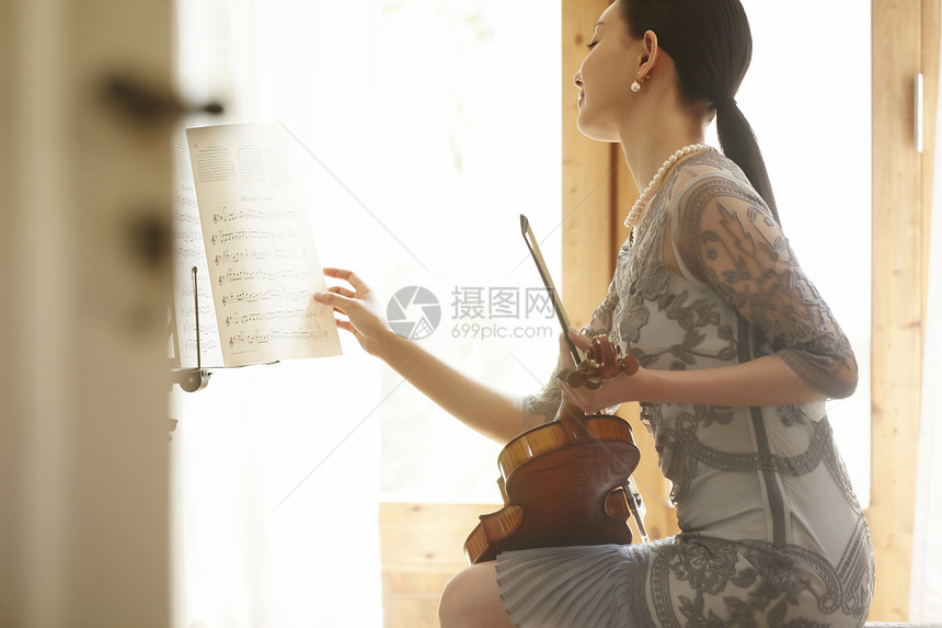 拿着小提琴翻阅着琴谱的优雅女性图片