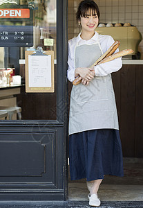站在门口抱着法式面包微笑的年轻女性图片