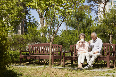 坐在公园长凳上喝茶休息的老夫妇高清图片