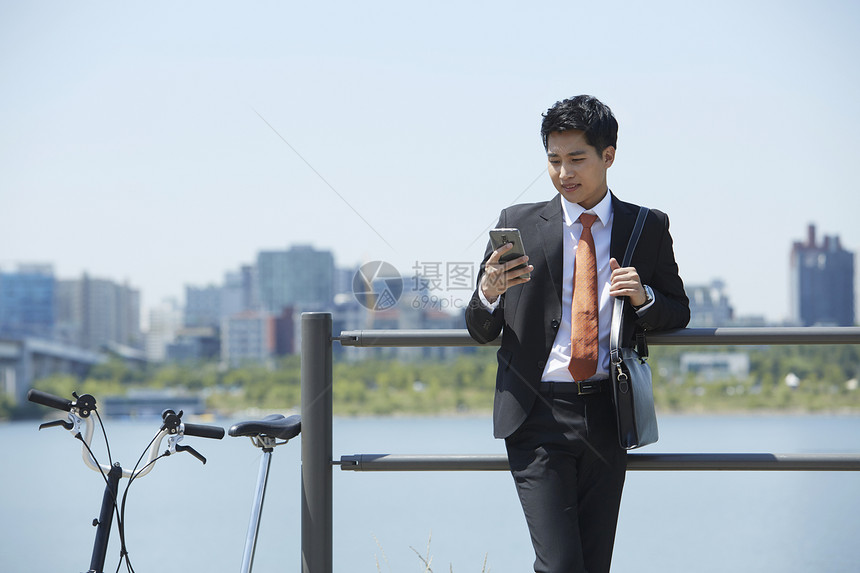 靠在湖边栏杆上拿着手机的男性图片