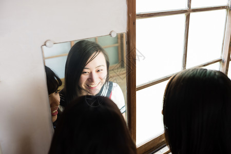 站在镜子前照镜子的女高中生木制高清图片素材
