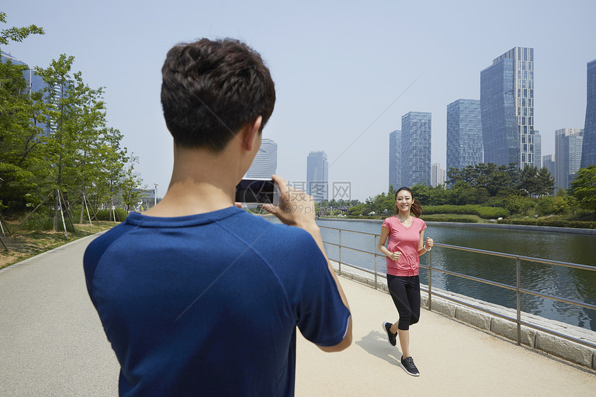 丈夫拿着手机拍跑步运动的妻子图片