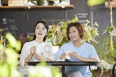 室内开心的母女坐一起喝咖啡看风景花高清图片素材