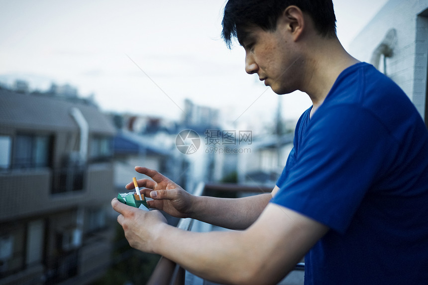 站在阳台拿着香烟的成年男子图片