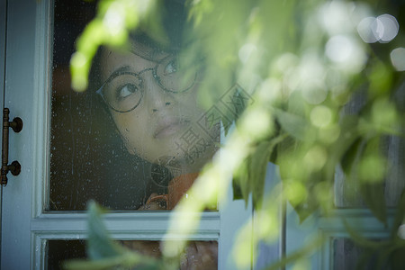 透过窗户看下雨的年轻女人假日高清图片素材